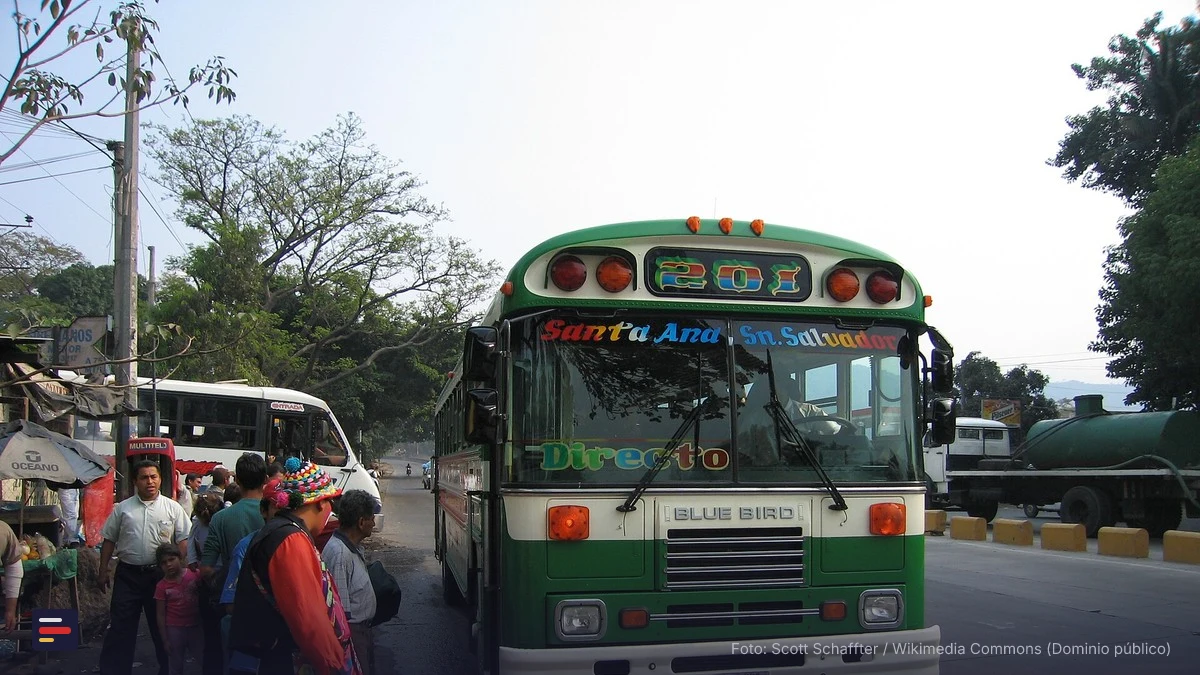 Bus de transporte público salvadoreño (school bus reciclado Blue Bird) circulando por una calle con pasajeros